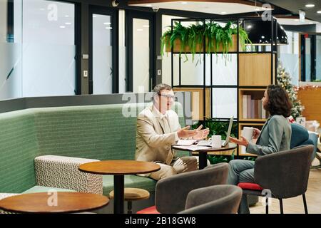 Reife Geschäftsleute treffen sich am kleinen Tisch in der Lounge im Büro und diskutieren Dokumente und Projektdetails Stockfoto