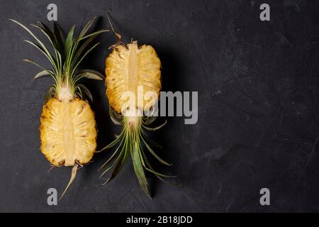 Zwei Hälften frisch geschnittener Ananas auf schwarzem Hintergrund, Draufsicht mit Kopierraum Stockfoto