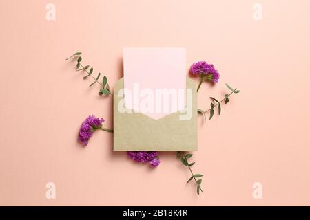 Kraft-Umschlag und leere Karte mit Statikblüte, Eukalyptusblätter auf pinkfarbenem Hintergrund. Blumendesign, flacher Lay, Draufsicht, Kopierbereich Stockfoto