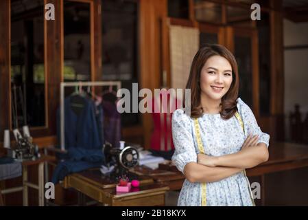 Schöne asiatische Dressurreiterin im Arbeitszimmer. Designerin hält Arme über den Lippen und schaut mit Lächeln auf die Kamera, während sie in der Werkstatt steht Stockfoto