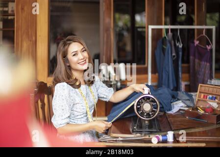 Schöne asiatische Dressurreiterin im Arbeitszimmer. Designerin hält Arme über den Lippen und schaut mit Lächeln auf die Kamera, während sie in der Werkstatt steht Stockfoto