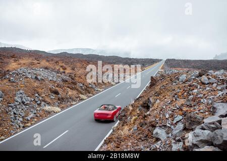 Blick auf die Landschaft auf der schönen geraden Straße im vulkanischen Tal mit einer Frau, die ein rotes Cabriolet fährt, weiter Blick von oben. Reisen mit dem Auto auf der Insel Tenera, Spanien Stockfoto