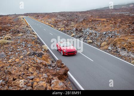 Blick auf die Landschaft auf der schönen geraden Straße im vulkanischen Tal mit einer Frau, die ein rotes Cabriolet fährt, weiter Blick von oben. Reisen mit dem Auto auf der Insel Tenera, Spanien Stockfoto