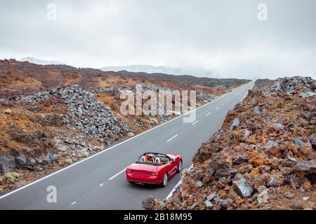 Blick auf die Landschaft auf der schönen geraden Straße im vulkanischen Tal mit einer Frau, die ein rotes Cabriolet fährt, weiter Blick von oben. Reisen mit dem Auto auf der Insel Tenera, Spanien Stockfoto