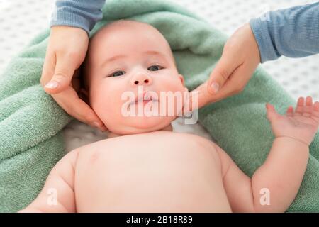 Gesichtsmassage für Babys. Mutter streichelt sanft mit beiden Händen das Gesicht des Babyjungen. Nahaufnahme mit zugeschnittenen Aufnahmen. Stockfoto