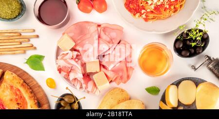 Italienische Kaltschnitte Panoramaaufnahme über dem Kopf. Eine Auswahl an Schinken und Käse, von oben auf weißem Hintergrund mit Wein geschossen Stockfoto