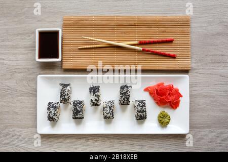 Ursprünglich legte Sushi Rolle auf einem weißen Teller. Mit Essstäbchen, Ingwer, Wasabi und Sojasauce auf einer weißen kleinen Schüssel Stockfoto