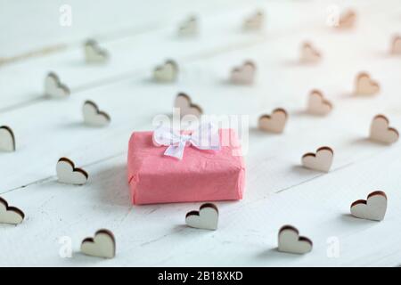 Kleines Geschenk in rosa Papier mit kleinen weißen Schleife auf Holz weißen Hintergrund eingewickelt. Stockfoto