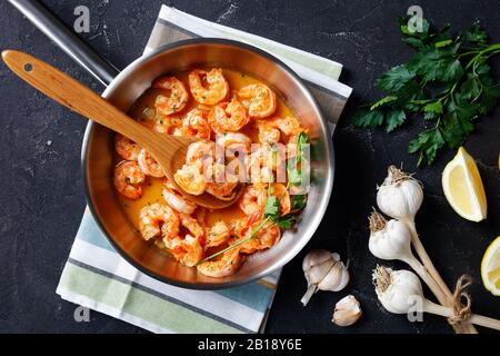 Garnelenschampi mit Knoblauchbuttersauce serviert mit Zitrone und mit Petersilie bestreut, auf einer Bratpfanne mit Zutaten auf einem Betongrund, Blick auf Friso Stockfoto