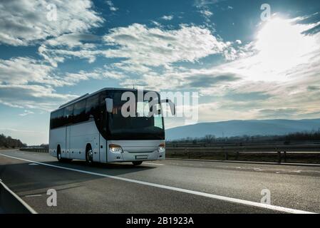 Weißer, Moderner, komfortabler Touristenbus, der bei strahlendem Sonnenschein durch die Autobahn fährt. Reise- und Reisebus-Tourismus-Konzept. Fahrt und Fahrt mit dem Fahrzeug Stockfoto