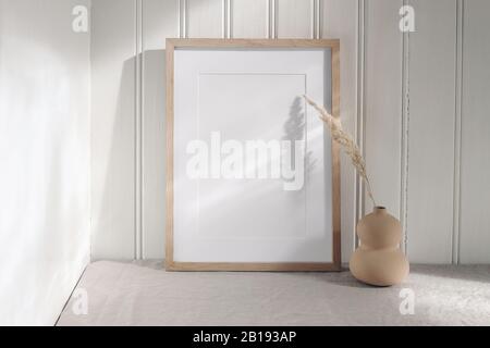 Portrait leerer Holzrahmen Mockup mit moderner Keramikvase, trockenem Gras bei Sonnenlicht, langen Schatten. Weiße Beadboard Wandverkleidung Hintergrund Stockfoto