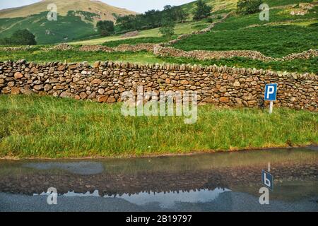 Trockenmauern und P für Parkschild, die sich in der Straßenpfütze, dem Kirkstone Pass, dem Lake District National Park, Cumbria, England widerspiegeln Stockfoto