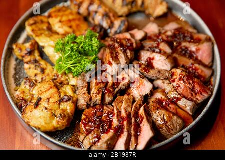 Frische, saftige Sortiment von geschnittenen Fleisch vom Grill, die auf eine große und runde Platte liegt, mit Petersilie auf der Oberseite dekoriert. Stockfoto