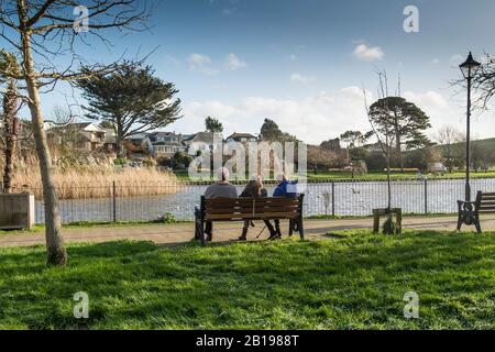 Entspannen Sie sich auf einer Bank mit Blick auf den See mit Bootstouren in den Trenance Gardens in Newquay in Cornwall. Stockfoto