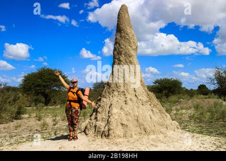 Riesiger Termitenhügel (anthill) in Afrika, Namibia. Ein junges weißes Mädchen Tourist Backpacket steht in der Nähe und zeigt, wie riesig der Termitenhügel ist. Stockfoto