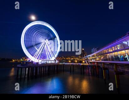 Beleuchtetes Riesenrad auf dem Pier in der Nacht im Mondlicht. Scheveningen, Den Haag auf dem Hintergrund, beliebtes touristisches Reiseziel. Stockfoto