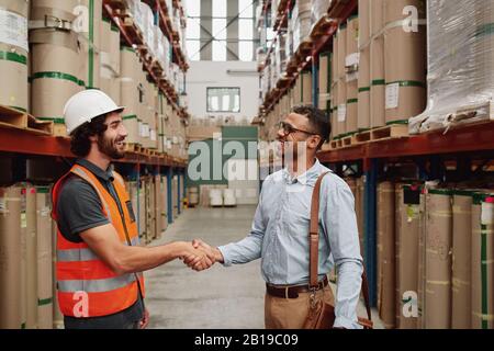 Fröhlicher junger Business man in formeller Kleidung, der einen Deal mit dem Lagerleiter macht - zwei Partner schütteln die Hände auf einen neuen Deal Stockfoto