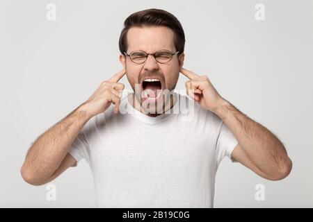Verärgert gestresster, tausendjähriger Kerl, der Ohren mit den Fingern verstopft. Stockfoto