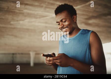 Ein afroamerikanischer Fit junger Mann, der Nachrichten auf dem Handy im Freien textet Stockfoto