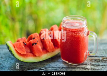 Glas Wassermelonen-Smoothie und ein Stück Wassermelone auf einem Holztisch Stockfoto