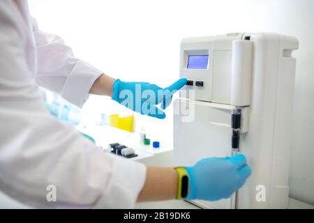 Techniker in blauen Handschuhen, der die Starttaste an der Kentifüge drückt Stockfoto