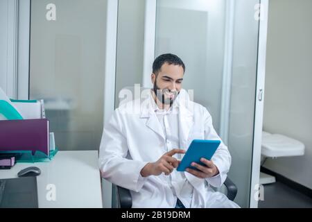 Männlicher Arzt in einer weißen Robe, der etwas im Internet liest Stockfoto