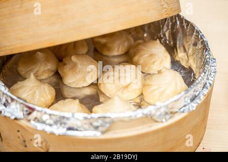 momo oder Knödel von oben, serviert in einem Bambusdampfer, der auf einer Holzoberfläche platziert ist. Stockfoto