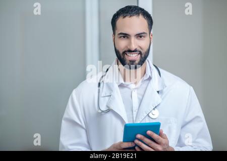 Männlicher Arzt in einer weißen Robe lächelnd und wohlfühlend Stockfoto