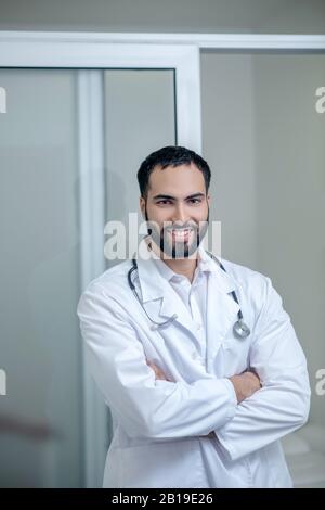 Männlicher Arzt in einem weißen Gewand, das mit gekreuzten Armen steht Stockfoto