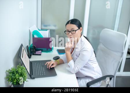 Dunkelhaarige weibliche Ärztin in Augenspülung, die nachdenklich aussieht Stockfoto
