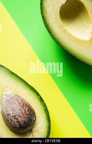 Bereit zum Essen Avocado in zwei Hälften geschnitten, isoliert auf grünem und gelbem Hintergrund. Stockfoto