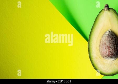Bereit zum Essen Avocado in zwei Hälften geschnitten, isoliert auf grünem und gelbem Hintergrund. Stockfoto