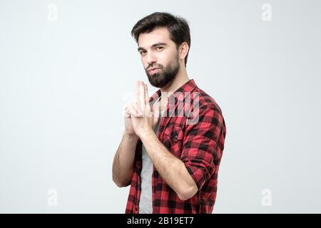 Kaukasisches Männchen mit dunklem Haar macht Gesichter, schaut ernsthaft auf die Kamera und gibt vor, Gewehr zu haben Stockfoto