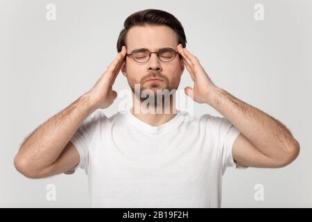 Gestresster junger Kerl in Brillen, die an Kopfschmerzen leiden. Stockfoto