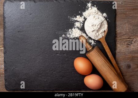 Background mit Eiern und Mehl auf schwarzem Hintergrund. Ansicht von oben. Kopierbereich Stockfoto