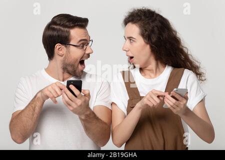 Stauntes glückliches junges Paar, das Mobiltelefone hält und auf den Bildschirm zeigt. Stockfoto