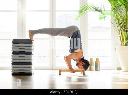 Muskulöser junger Mann, der ein Kalisthenik-Workout durchführt, indem er V-Push-Ups auf Low-Floor-Bars vor einer hellen Fensterkulisse in einem gesunden Lebensstil und einer gesunden FI ausführt Stockfoto