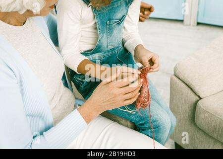 Großmutter Und Kind Stricken Zu Hause Closeup Der Hübschen Kleinen Blonde Lady Stritting Und Ihrer Großmutter, Die Sie Anschaut, Und Helfen Ihrer Kleinen Dame Kn Stockfoto