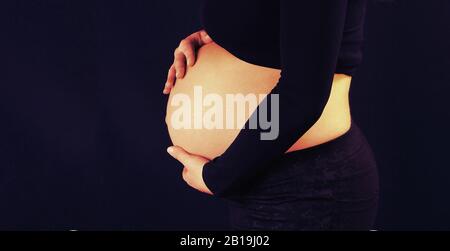 Schwangere Frau im fortgeschrittenen Schwangerschaftszustand mit den Händen auf dem Bauch. Stockfoto