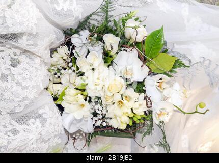 Bouquet von weißen Rosen und Orchideen auf einem weißen Spitzenstoff. Stockfoto