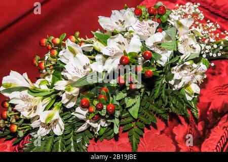 Bouquet von weißen Lilien mit Flecken und roten Früchten auf rotem Tuch. Lilium 'Stargazer. Stockfoto