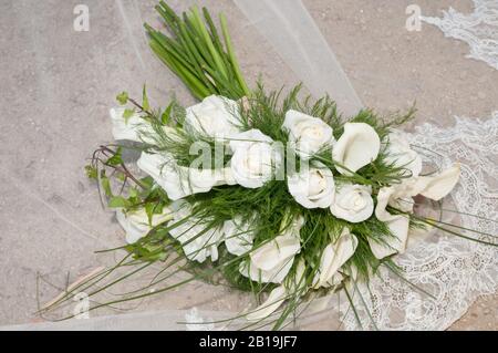 Blumenstrauß aus Calla und weißen Rosen auf dem Schleier einer Braut auf dem Boden. Zantedeschia aethiopica. Tölpel. Rosen Stockfoto