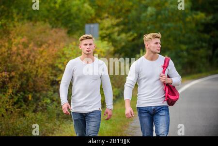 Zwillinge gehen auf der Straße. Abenteuerkonzept. Jungs hitchwander auf der Straße. Touristenreisende fahren mit Auto. Probleme beim Transport. Stelle auswählen, an der das Auto leicht zur Seite ziehen kann. Männer Rucksack Laufstraße. Stockfoto