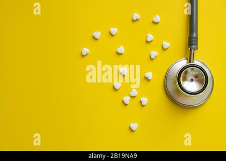 Medizinisches Stethoskop und weiße Herzpillen auf gelbem Hintergrund Gesundheitsminimalismuskonzept Stockfoto