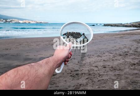 Der junge Mann, der Mikroplastiken aus Sand am Strand reinigt - Umweltproblem, Umweltverschmutzung und Ökolosystem-Warnkonzept - Liegt Im Fokus Stockfoto