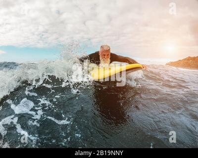 Senior Mann surft mit Longboard auf einer Welle - Fröhlicher alter Kerl, der Spaß am Extremsport hat - Fröhliches älteres Konzept - Konzentriert sich auf sein Gesicht Stockfoto