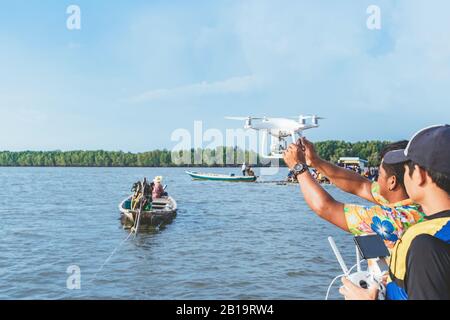 Junger Mann in blau-gelber Lebensweste, der eine Drohne kontrolliert, um mit Touristen auf einem Floß im Meer Bilder von der Küste des Ozeans zu machen. Hände h Stockfoto