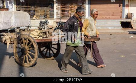 Jamnagar, Gujarat, Indien - Dezember 2018: Zwei Arbeiter ziehen ihren Holzwagen auf den Marktstraßen der Stadt. Stockfoto