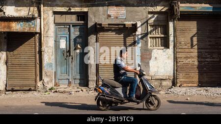 Jamnagar, Gujarat, Indien - Dezember 2018: Die verschlammten Fenster der Geschäfte auf dem Markt auf einem Urlaub. Ein Mann auf einem Roller fährt auf den Straßen vorbei. Stockfoto