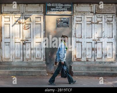 Jamnagar, Gujarat, Indien - Dezember 2018: Ein Mann geht an den weißen, verschlossenen, hölzernen Türen eines Ladens auf den Straßen der Altstadt vorbei. Stockfoto